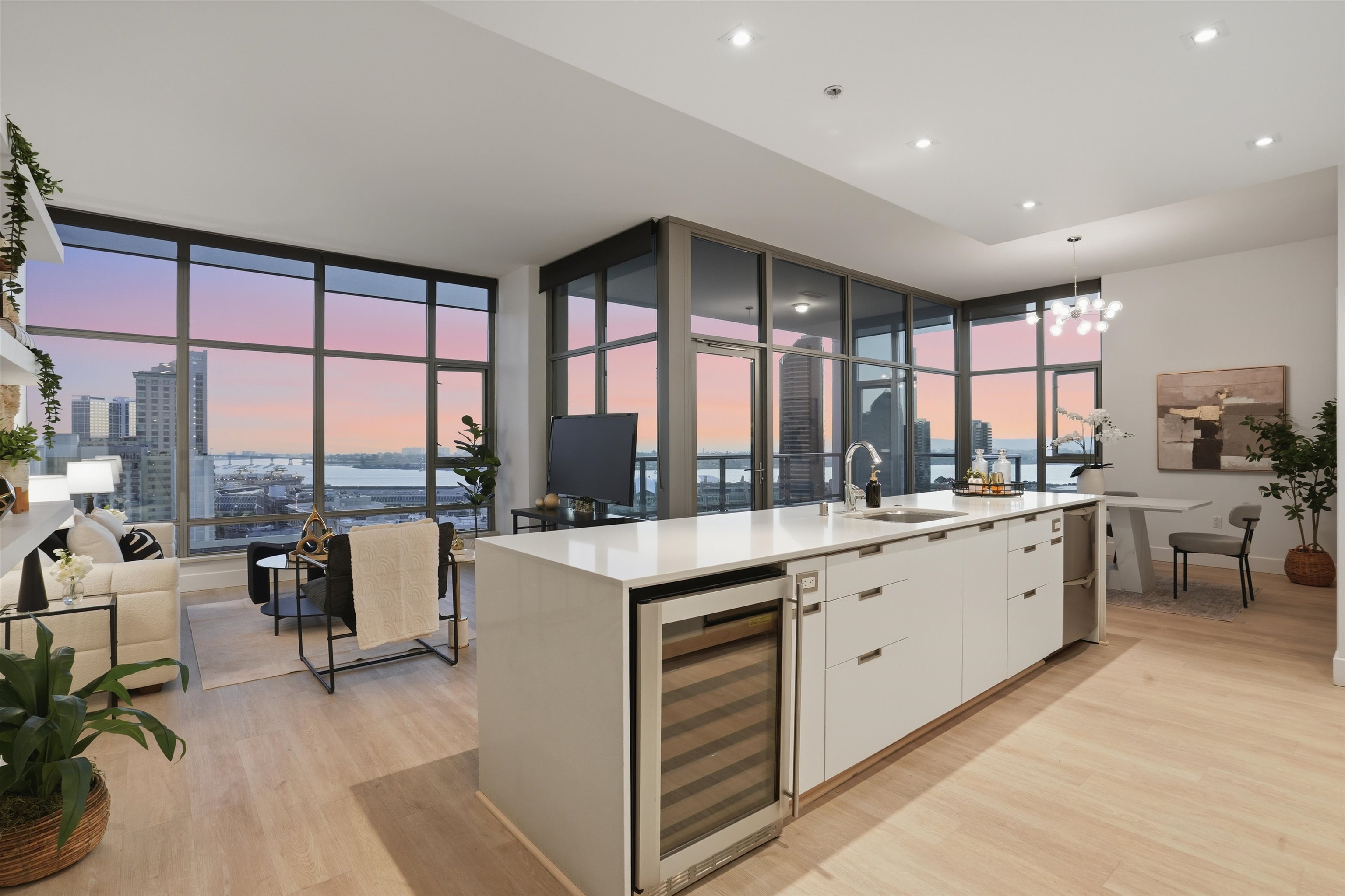 Living and kitchen space at 575 6th Ave #1705 on the seventeenth floor of The Alta, with floor-to-ceiling glass framing the downtown San Diego skyline and bay at sunset